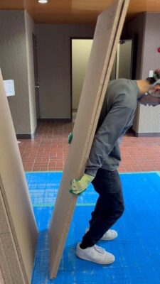 大東市の建築現場で養生シートを敷いた通路を通り、木材やボード系資材を丁寧に搬入している荷揚げ作業の様子
