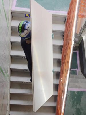 交野市の建築現場で階段を使って板状資材を慎重に搬入する荷揚げ作業